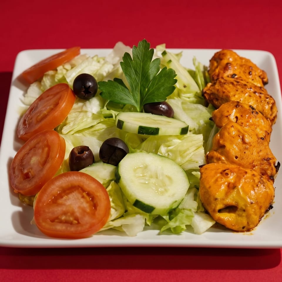Chicken tikka skewers with a side salad of lettuce, tomatoes, cucumbers, olives, and parsley.
